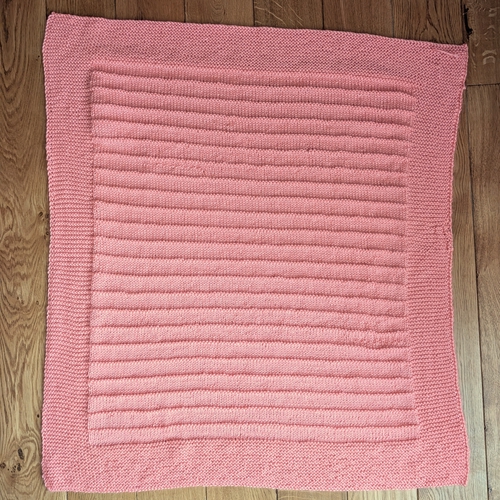 Square, pink knitted baby blanket with garter stitch border and purl stripes